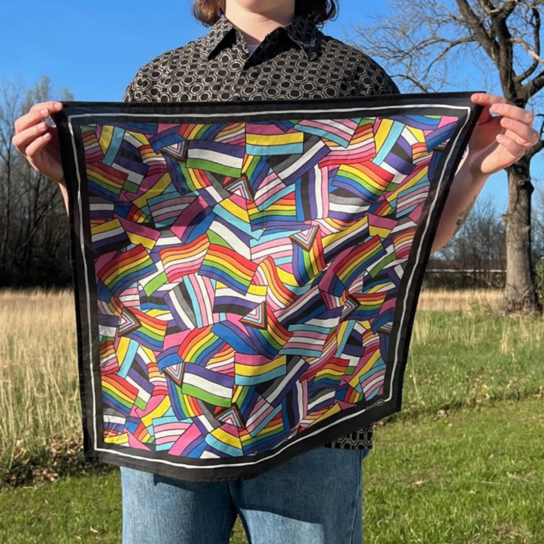 A black bandana featuring a pattern of overlapping Pride flags in various colors and designs. The flags include the classic rainbow flag, the transgender flag, and the bisexual flag.