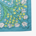 A blue bandana with a floral pattern. The pattern features white flowers with yellow centers and green leaves. The border of the bandana has a decorative, repeating pattern.