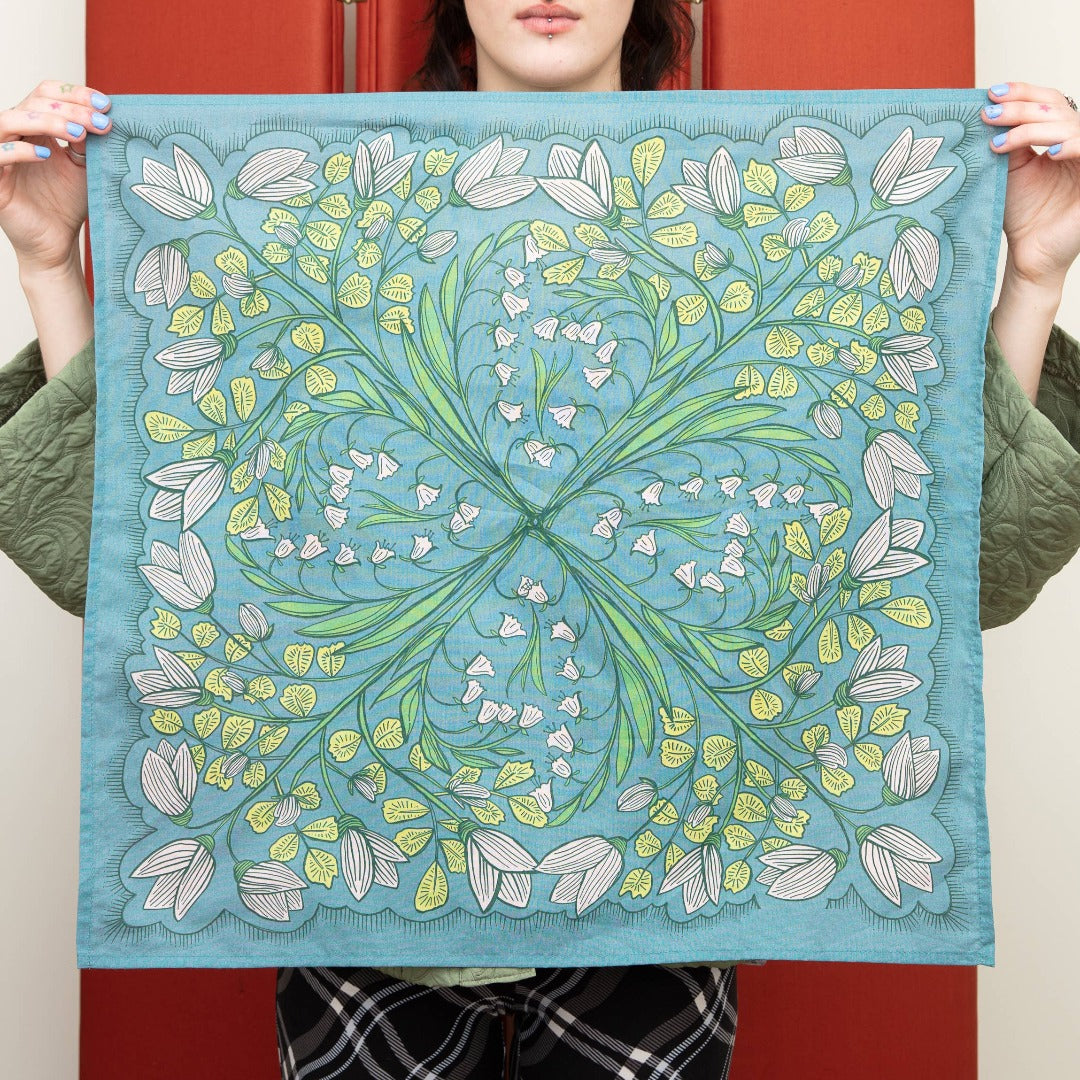 A blue bandana with a floral pattern. The pattern features white flowers with yellow centers and green leaves. The border of the bandana has a decorative, repeating pattern.