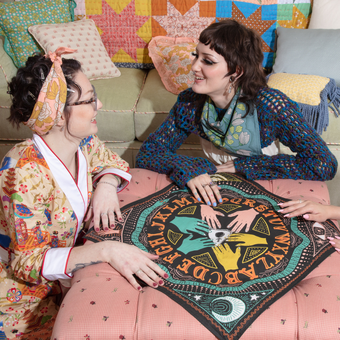 A black bandana with a mystical pattern. The pattern features a Ouija board design with hands pointing to letters and numbers, along with celestial symbols like moons and stars.