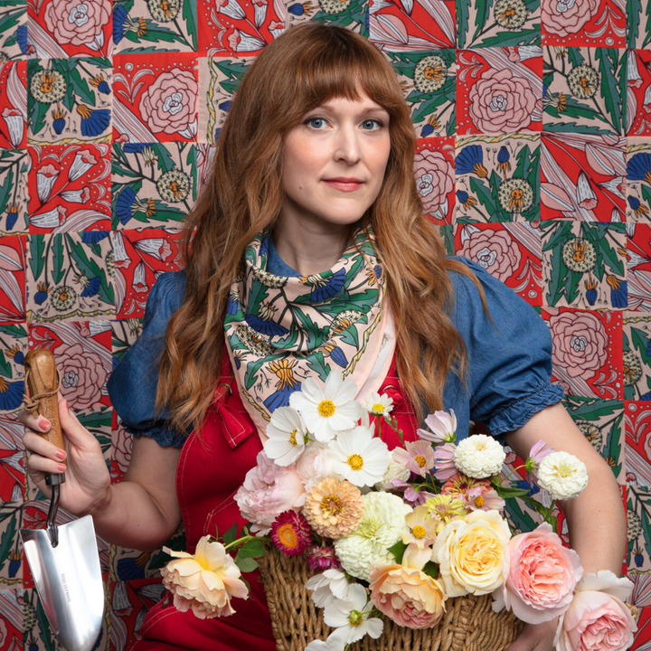 A pink bandana with a floral pattern. The pattern features blue and yellow dandelions with green leaves. The border of the bandana has a decorative, repeating pattern.