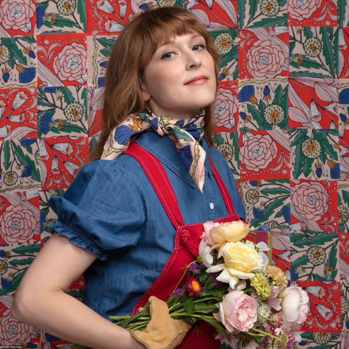 A pink bandana with a floral pattern. The pattern features blue and yellow dandelions with green leaves. The border of the bandana has a decorative, repeating pattern.