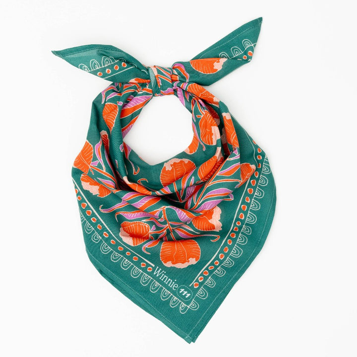 A green bandana with a floral pattern. The pattern features orange and pink flowers with green leaves. The border of the bandana has a decorative, repeating pattern.