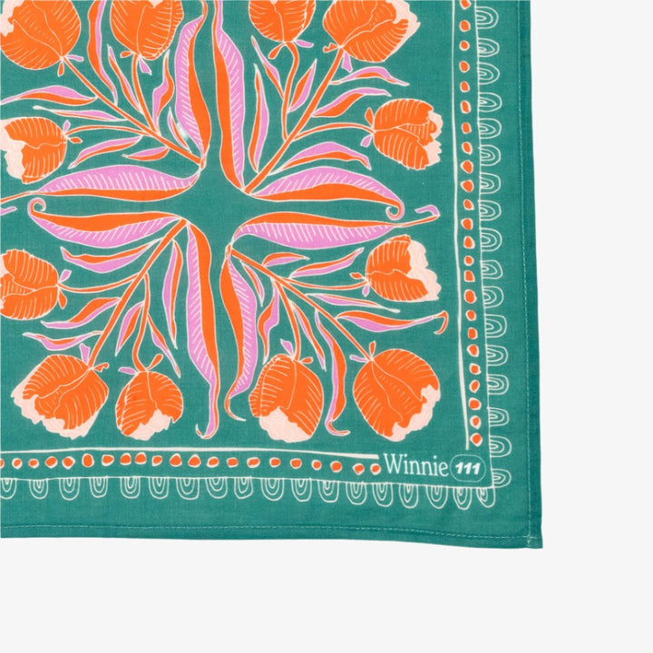 A green bandana with a floral pattern. The pattern features orange and pink flowers with green leaves. The border of the bandana has a decorative, repeating pattern.