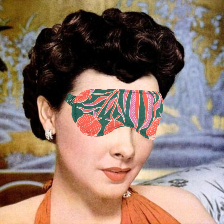 A green sleep mask with a floral pattern. The pattern features pink flowers and green leaves on a green background. The mask has an elastic band to fit around the head.