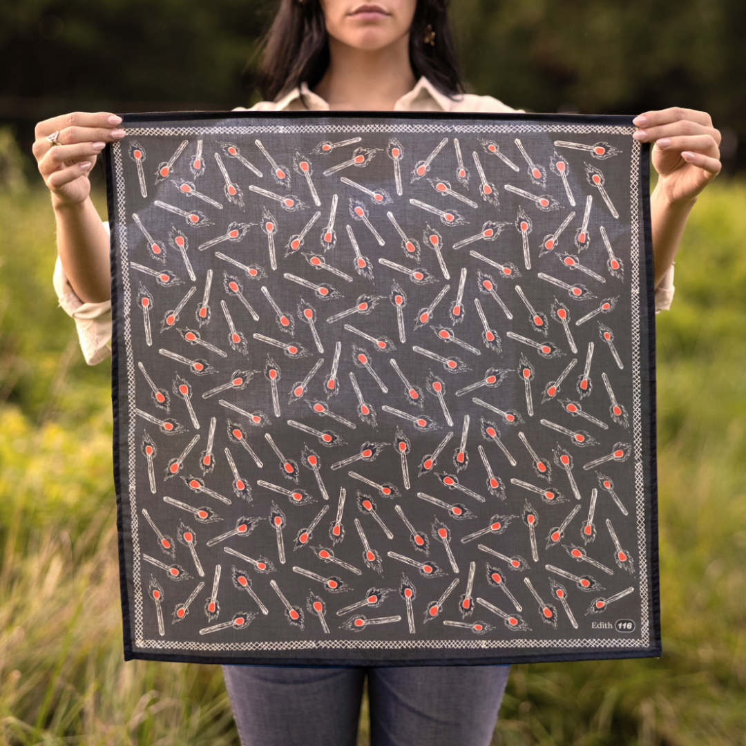 Person holding a black fabric with red and white pattern in a grassy outdoor setting