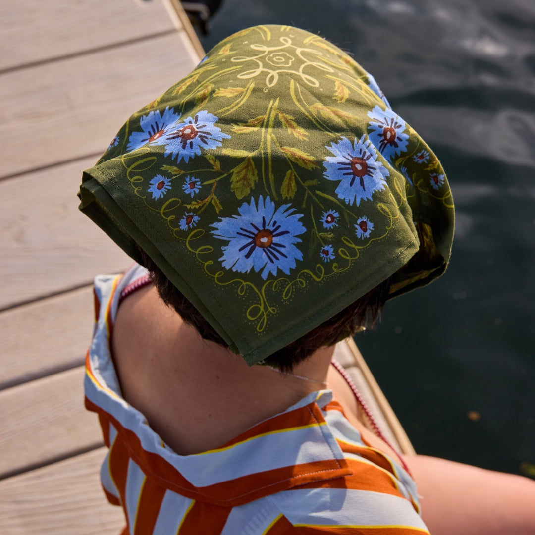 Person wearing a floral-patterned green headscarf by a body of water