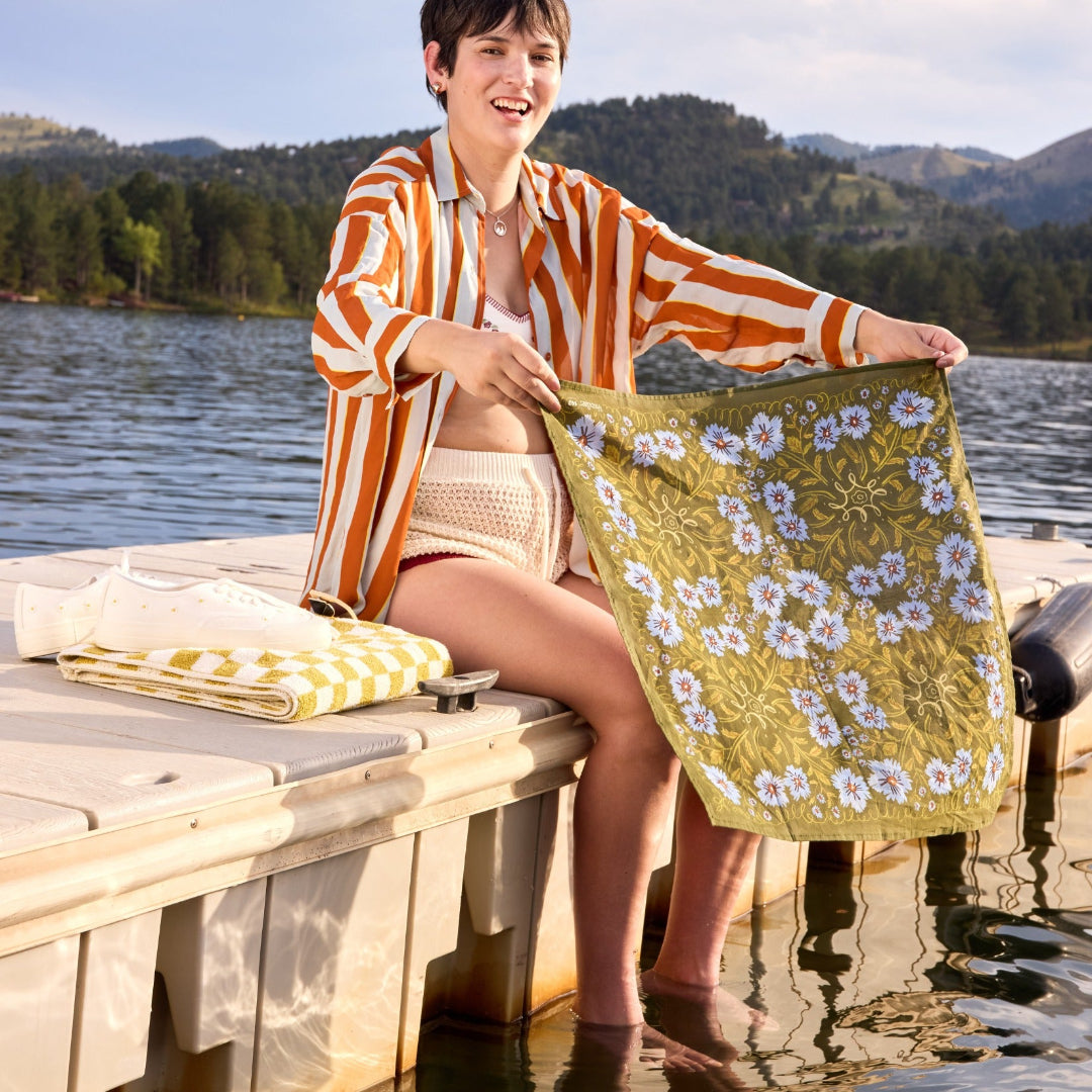 Woman holding a floral towel by a lake with mountains in the background
