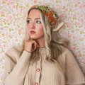 Woman wearing a beige cardigan and colorful headscarf against a floral wallpaper background