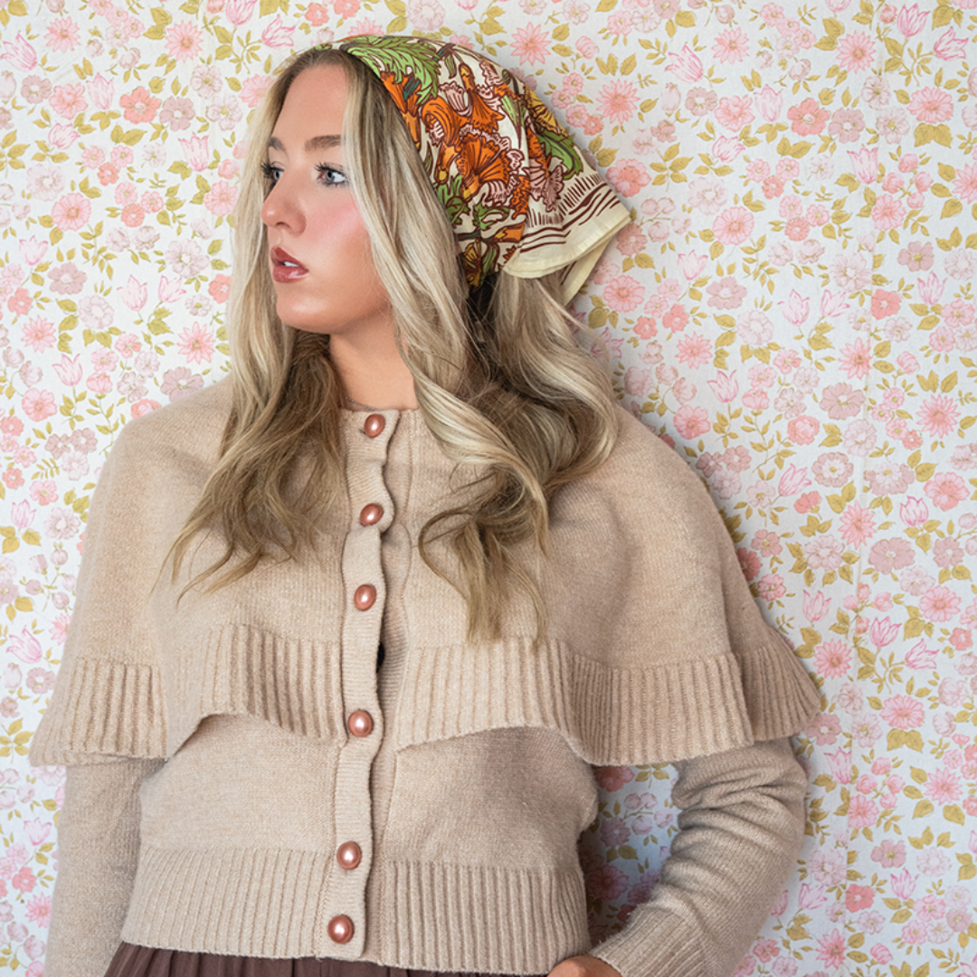Woman wearing a beige cardigan and patterned headscarf against a floral wallpaper background