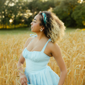 Woman in a light blue dress holding a floral clutch in a wheat field
