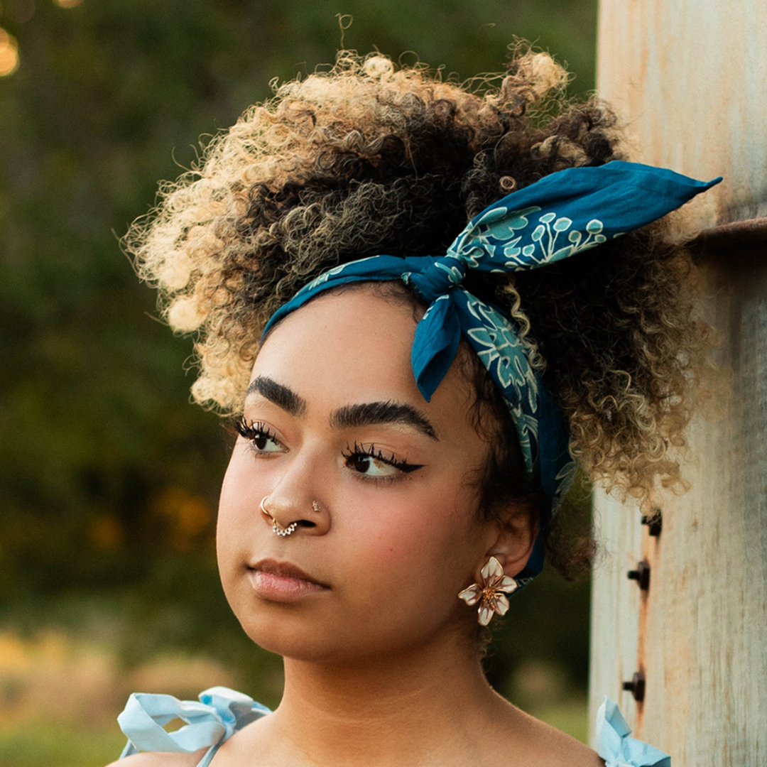 Woman with curly hair wearing a blue headscarf, standing outdoors.
