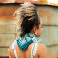 Woman with styled hair wearing a blue bandana with white patterns against a rustic wall.