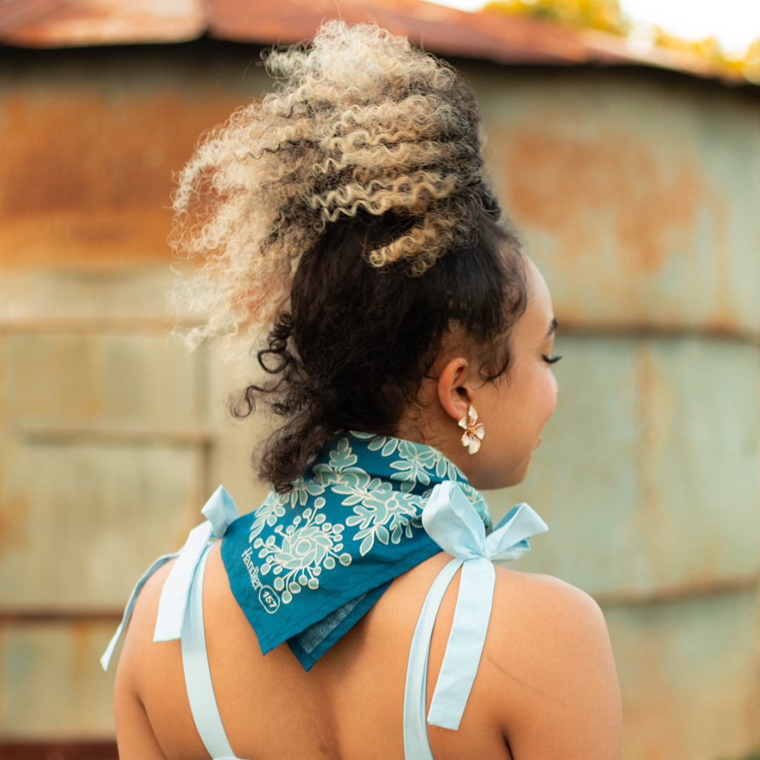Woman with styled hair wearing a blue bandana with white patterns against a rustic wall.