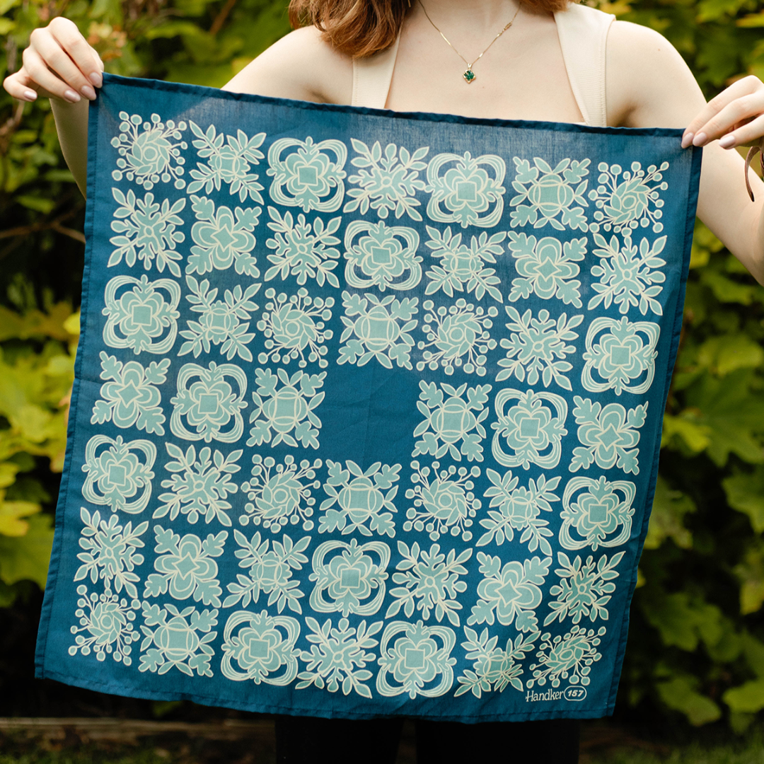 Person holding a blue fabric with white floral patterns against a green leafy background