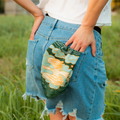 Person wearing denim shorts with a floral patch in a grassy outdoor setting