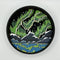A Paint By Layers Craft Kit featuring a circular shadow box with a pre-designed landscape scene. The scene depicts a mountain range under a vibrant aurora borealis. The kit includes layers of wood, paint, and instructions. The title of the kit is 