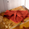 Knitted orange scarf on a wooden surface with a white background