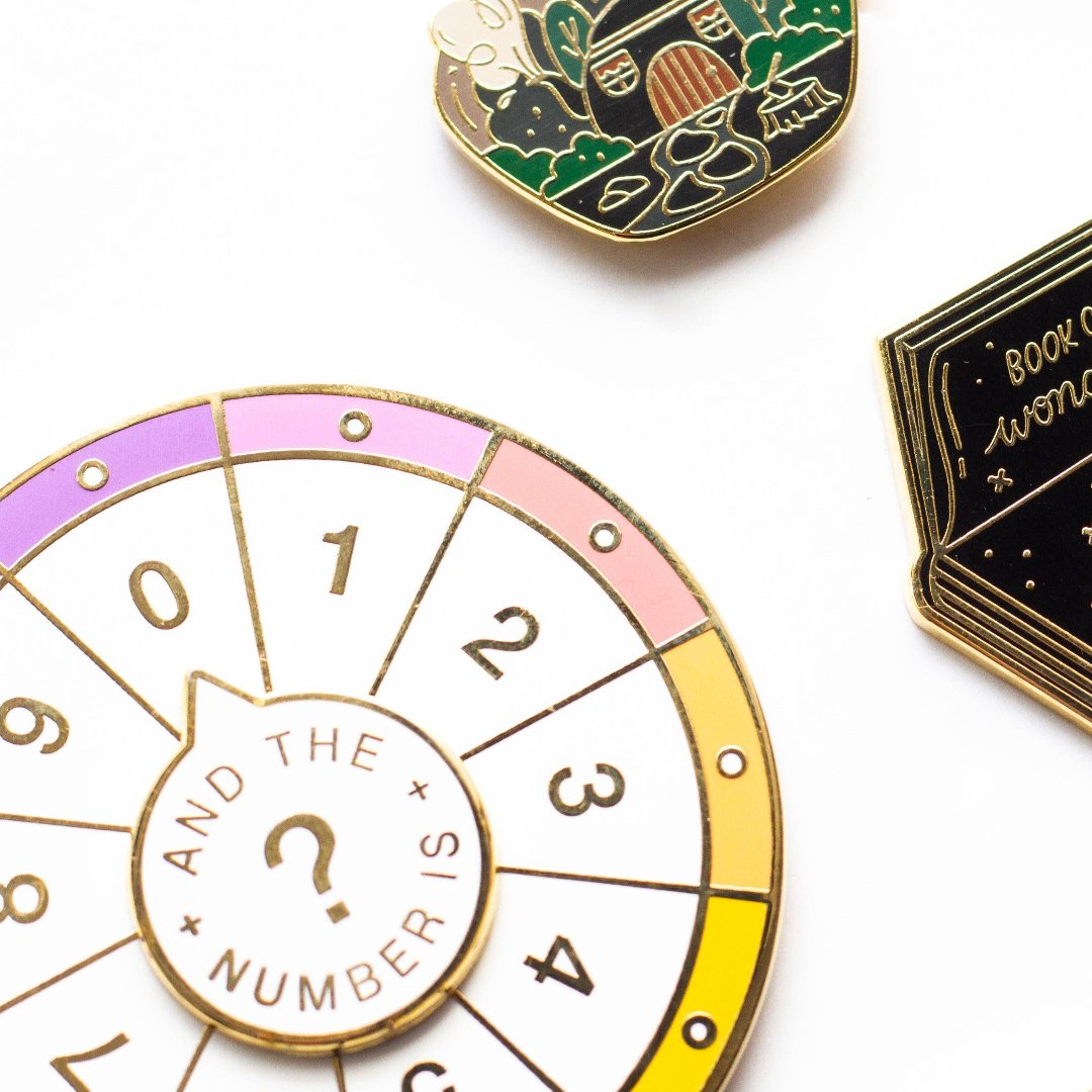 A circular pin with a colorful wheel featuring numbers from 0 to 9. The phrase "And the Numbers" is written in the center.