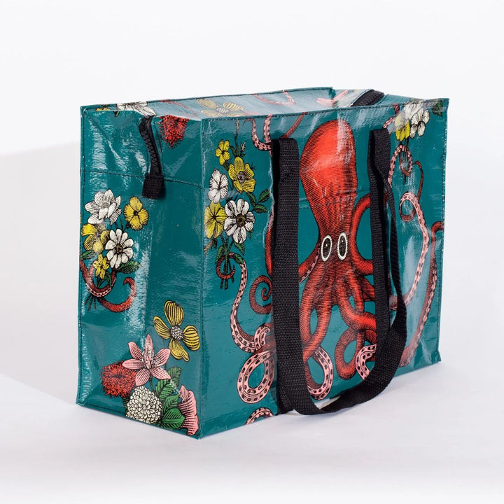 A rectangular shoulder tote bag with black handles, featuring a large red octopus with swirling tentacles against a teal background, surrounded by yellow and white flowers.