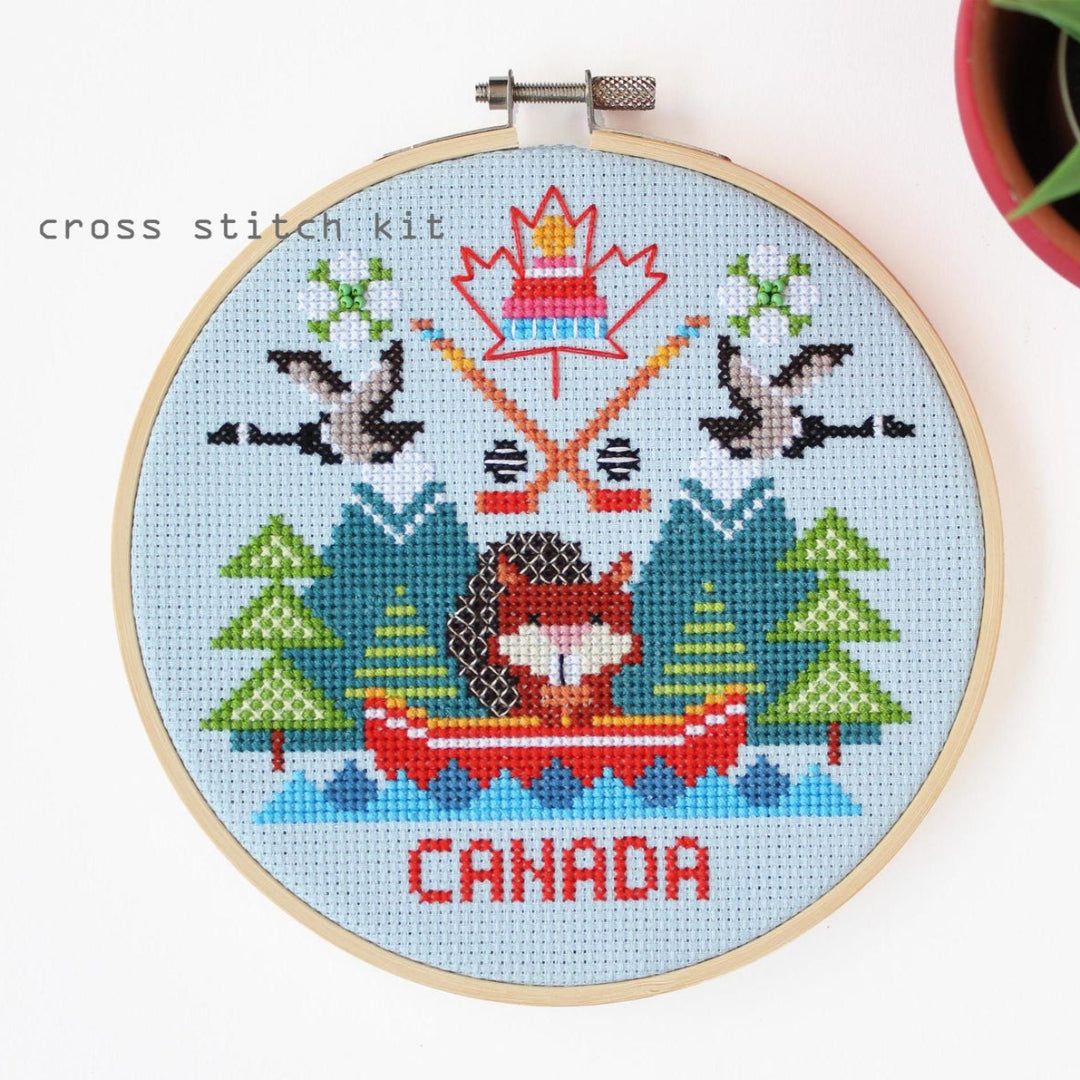Cross stitch kit with a design of a person in a canoe, trees, and the word 'Canada' on a blue background.