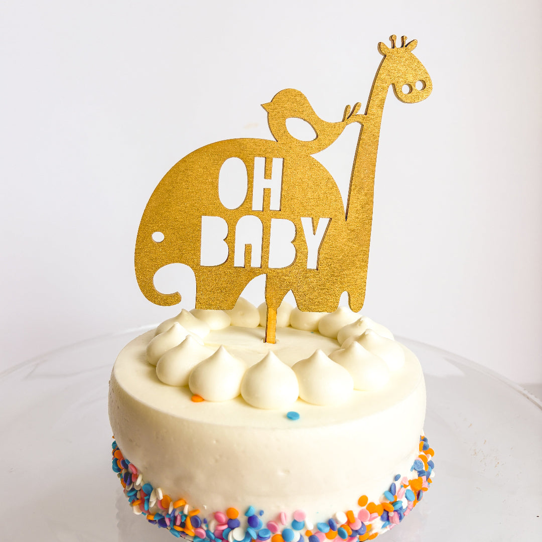 White cake with colorful sprinkles and 'OH BABY' topper on a white background