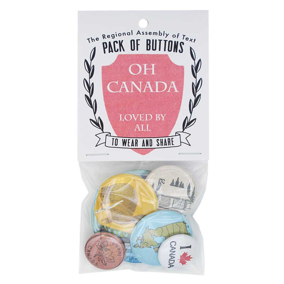 A clear plastic package containing six Canadian-themed pin-back buttons. The header card reads "The Regional Assembly of Text PACK OF BUTTONS" with a red shield containing "OH CANADA LOVED BY ALL" and "TO WEAR AND SHARE" below. Visible buttons include a maple leaf coin design, a globe with "I ♥ CANADA", and a cabin in a forest.
