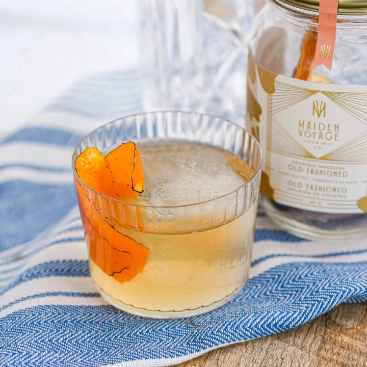 A glass jar filled with dried orange slices, dried cherries, and other ingredients. The jar has a white label with the Maiden Voyage logo and the product name 