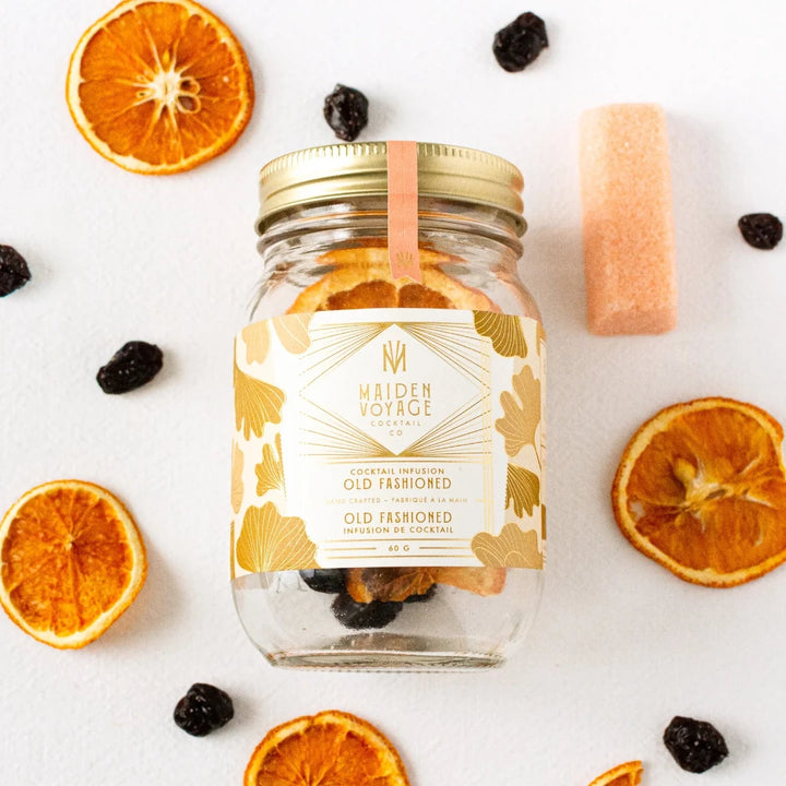 A glass jar filled with dried orange slices, dried cherries, and other ingredients. The jar has a white label with the Maiden Voyage logo and the product name 