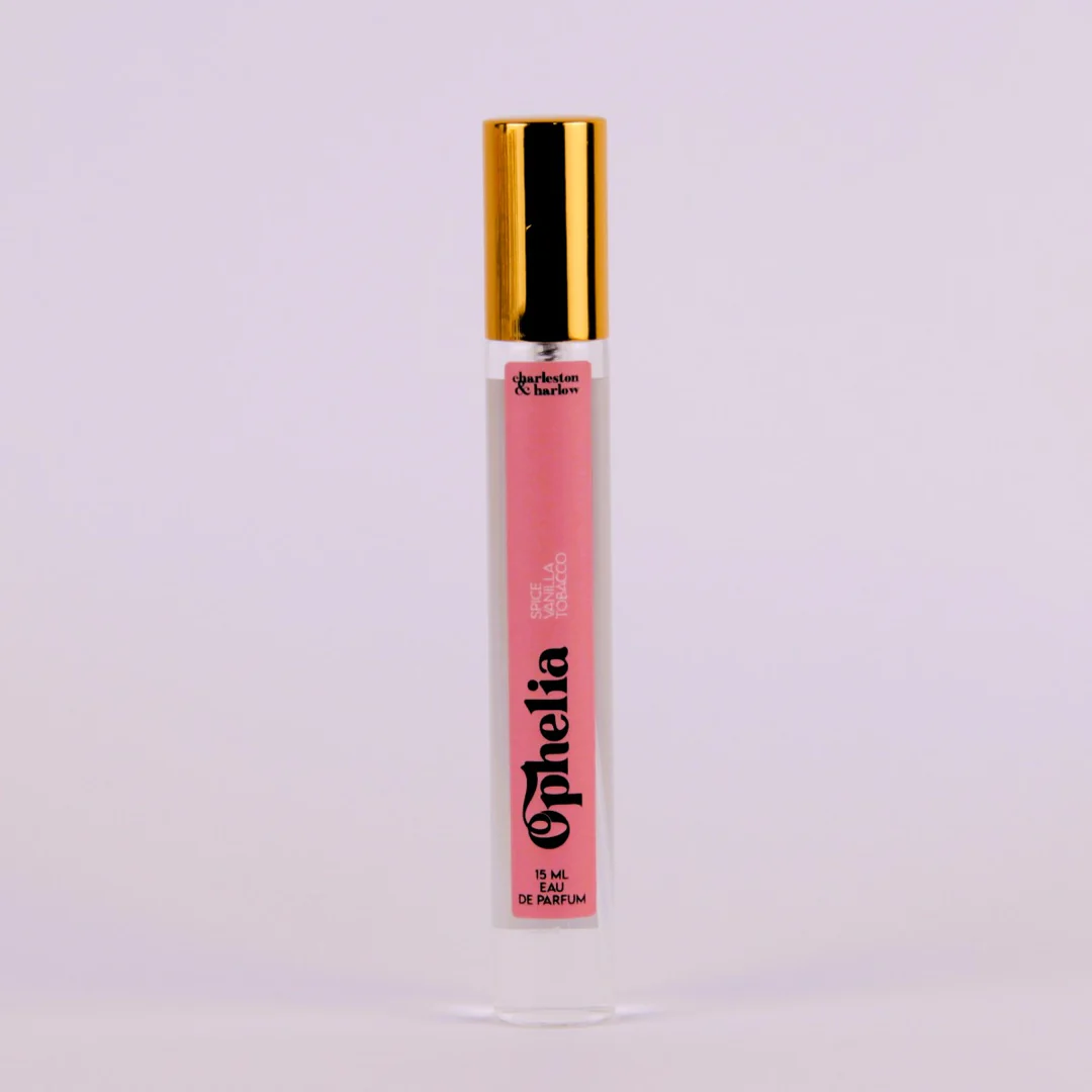 A bottle of Charleston & Harlow perfume named "Ophelia." The bottle is clear glass with a gold spray cap. The label is pink with the brand name and perfume name in a bold, playful font. The fragrance notes are listed as "Spice, Vanilla, Tobacco."