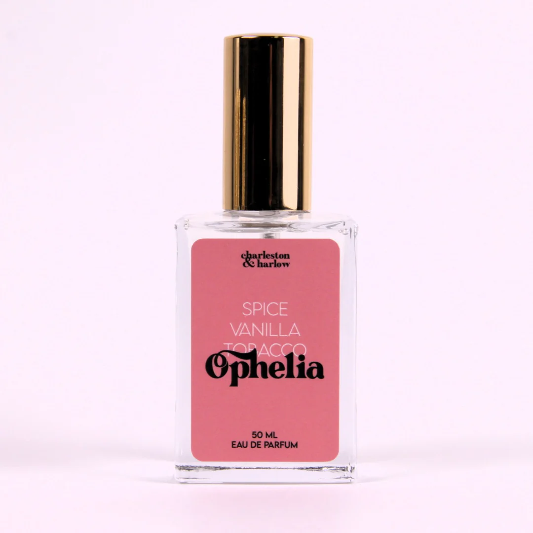 A bottle of Charleston & Harlow perfume named "Ophelia." The bottle is clear glass with a gold spray cap. The label is pink with the brand name and perfume name in a bold, playful font. The fragrance notes are listed as "Spice, Vanilla, Tobacco."
