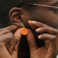 Person wearing a small orange earring with a green leaf.
