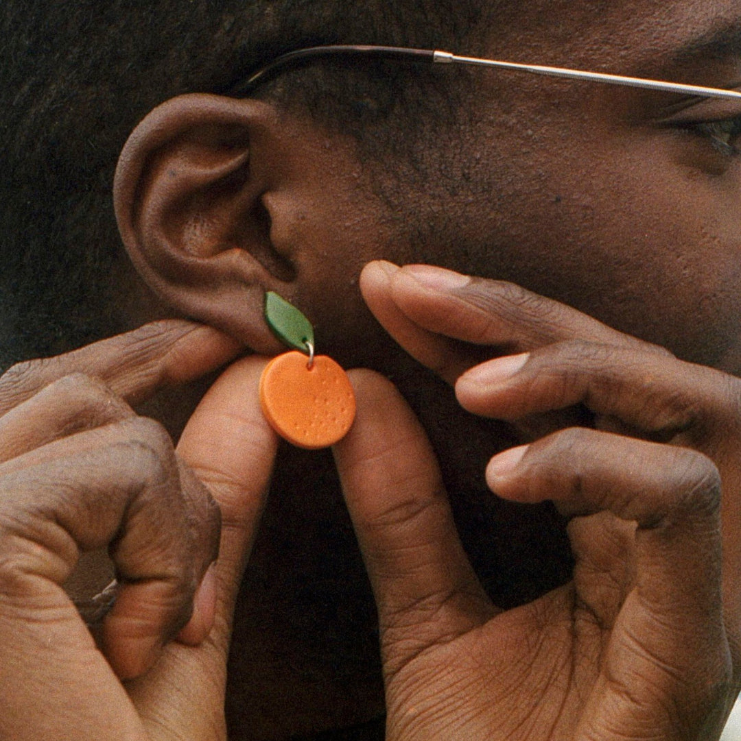 Person wearing a small orange earring with a green leaf.