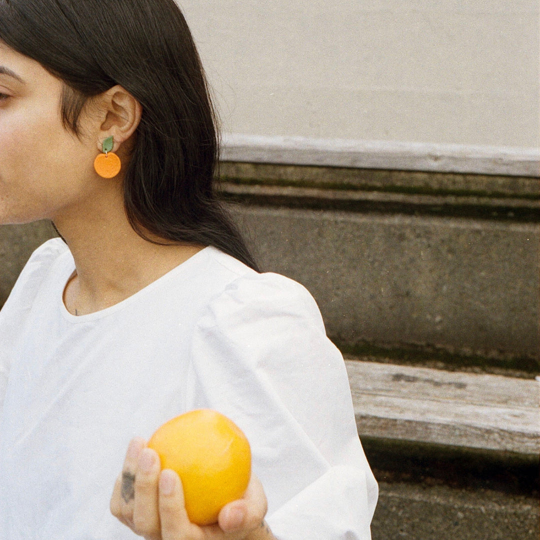 Woman holding an orange against a neutral background