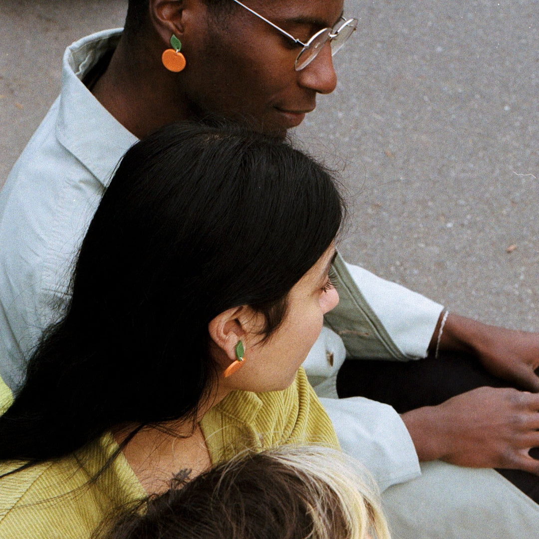 Two adults sitting on a bench with a child on their lap, all wearing earrings.