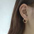 A pair of organic oval stud earrings made of gold fill, featuring a free-form, slightly irregular oval shape with a hammered texture, displayed on a textured ceramic surface. These modern earrings are available in Ottawa, Ontario, Canada.
