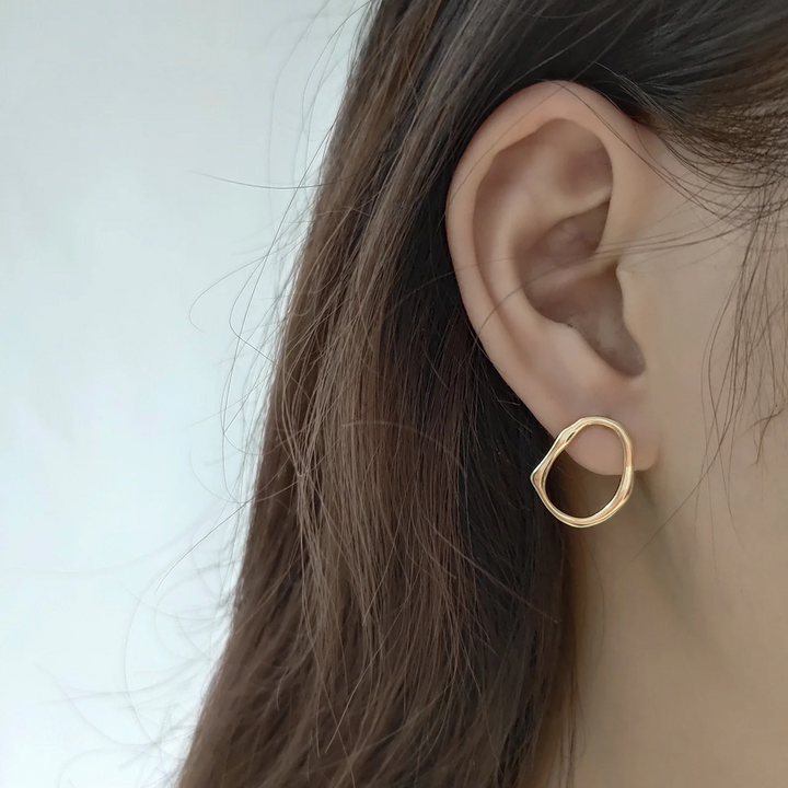 A pair of organic oval stud earrings made of gold fill, featuring a free-form, slightly irregular oval shape with a hammered texture, displayed on a textured ceramic surface. These modern earrings are available in Ottawa, Ontario, Canada.