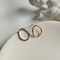 A pair of organic oval stud earrings made of gold fill, featuring a free-form, slightly irregular oval shape with a hammered texture, displayed on a textured ceramic surface. These modern earrings are available in Ottawa, Ontario, Canada.