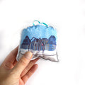 Hand holding a small fabric ornament with a cityscape design on a white background