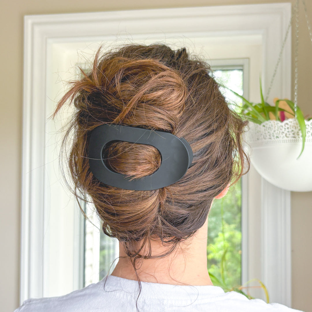 Person with a large black hair clip in their updo, with a window and plant in the background.