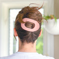 Person with a pink hair clip in their bun against a blurred indoor background