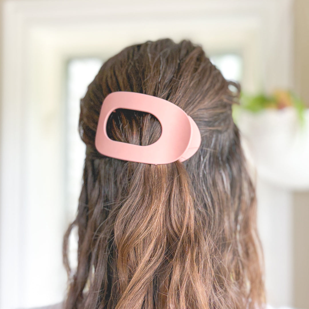 Person with a pink hair clip in their hair against a blurred indoor background