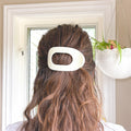 Person with a white hair clip in their brown hair, with a blurred indoor background