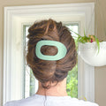 Person with a green hair clip in their bun, standing in front of a window.