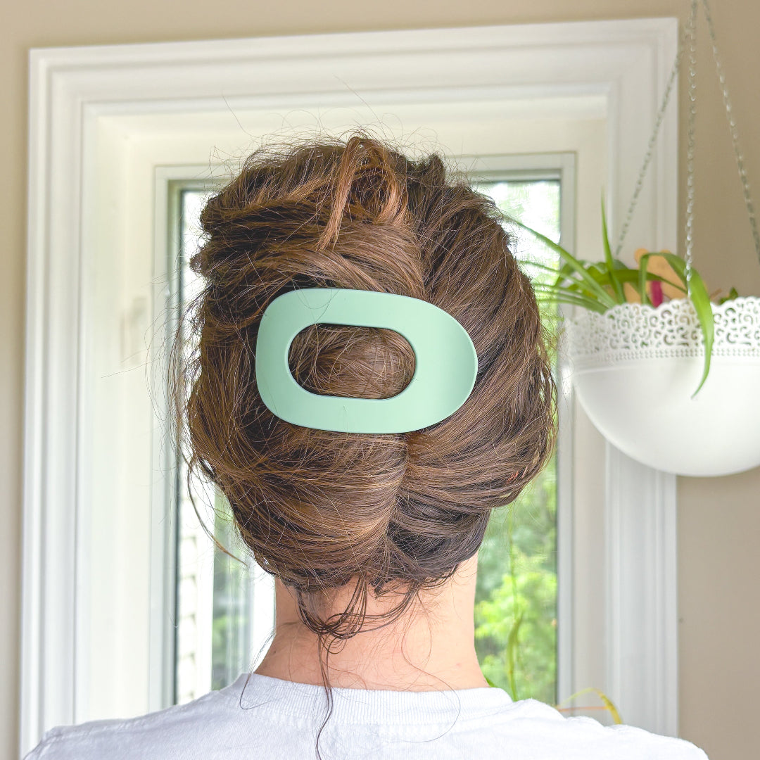 Person with a green hair clip in their bun, standing in front of a window.