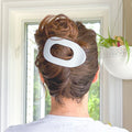 Person with a stylish hairdo featuring a large white hair clip, set against a neutral indoor background.