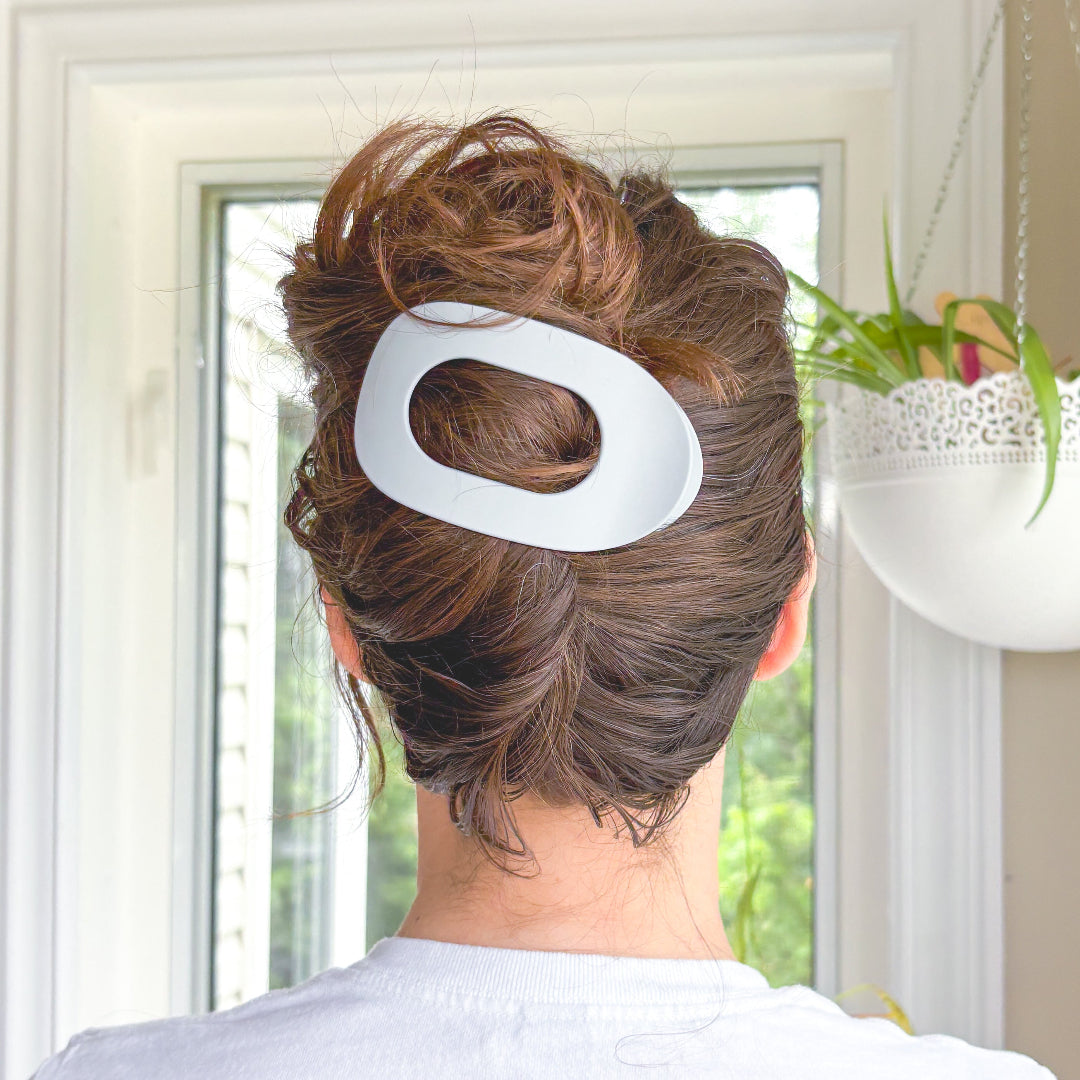 Person with a stylish hairdo featuring a large white hair clip, set against a neutral indoor background.