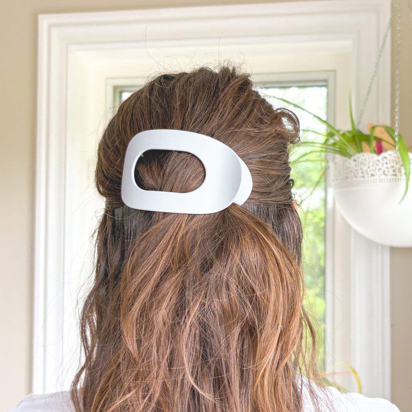 Person with a white hair clip in their brown hair indoors.