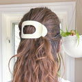 Close-up of a person with long brown hair wearing a white hair clip.