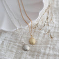 Two necklaces, one gold and one silver, on a textured surface with a white dish in the background.